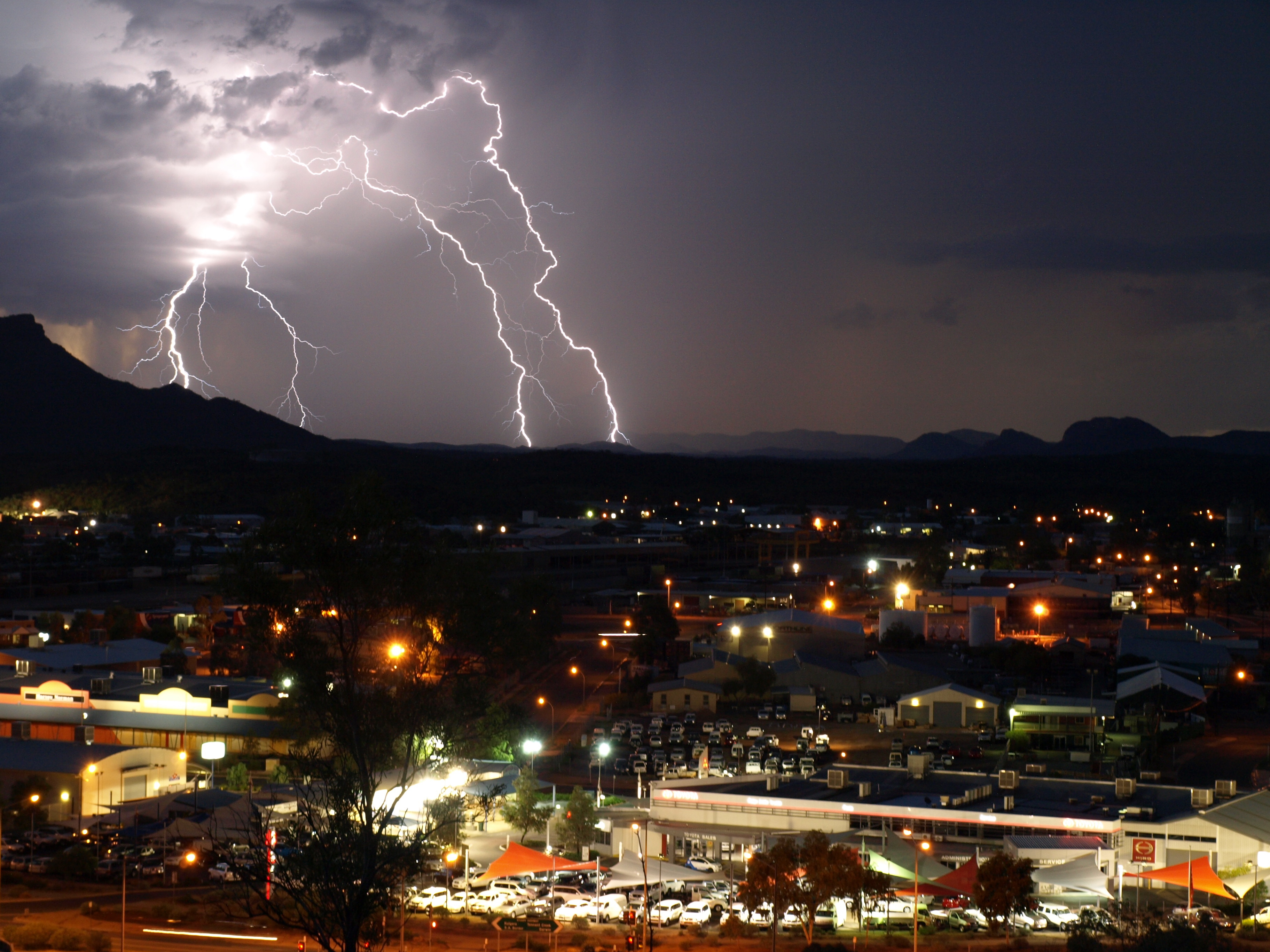 Multiple lightning bolts flash behind a town at night.