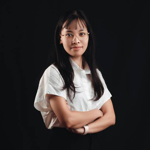 A woman in glasses and a white shirt stands with arms crossed.