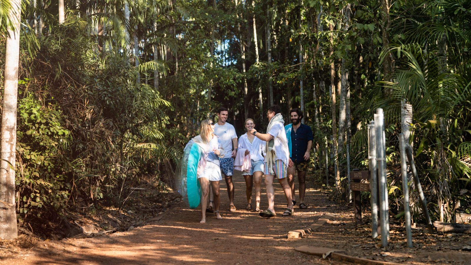 A group of friends walking along a bush track with a pool float at Berry Springs