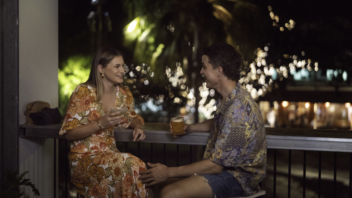 Woman in orange dress holding a drink and sitting with a man enjoying a drink on the terrace of Darwin Restaurant, Bar and Distillery in Darwin Citynt, Bar and Distillery in Darwin City