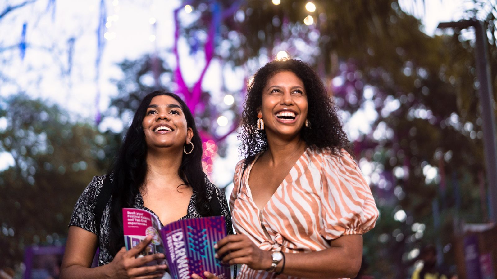 Two people holding a festival guide at Darwin Festival under decorative lights