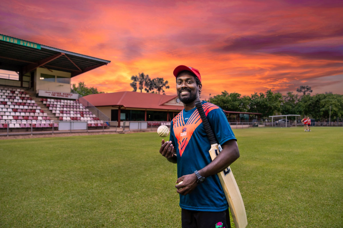 Man with cricket bat and ball training at sunset on Tracy Village grounds in Darwin