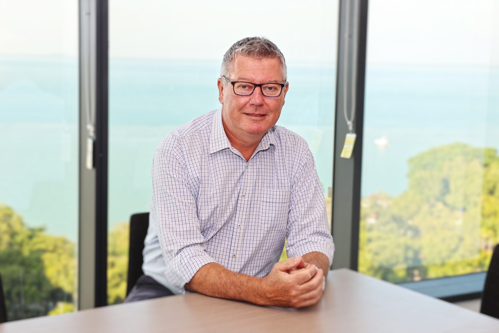 Man in glasses sitting at a desk with ocean view background.