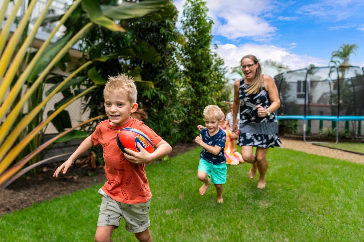 Mum with kids playing with football in tropical Darwin backyard