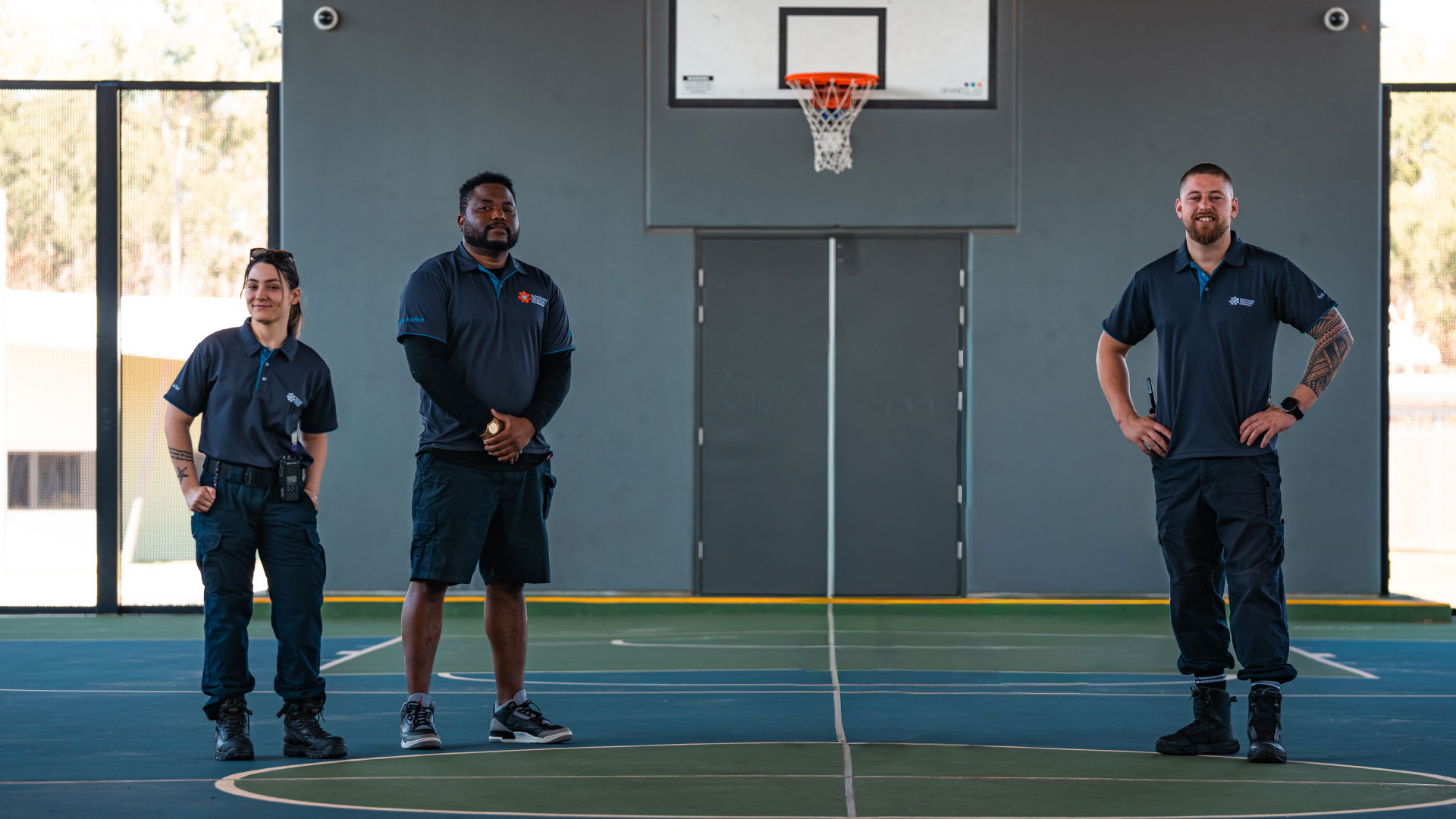 Three NT Corrections Youth Justice Officer standing on a basketball court smiling
