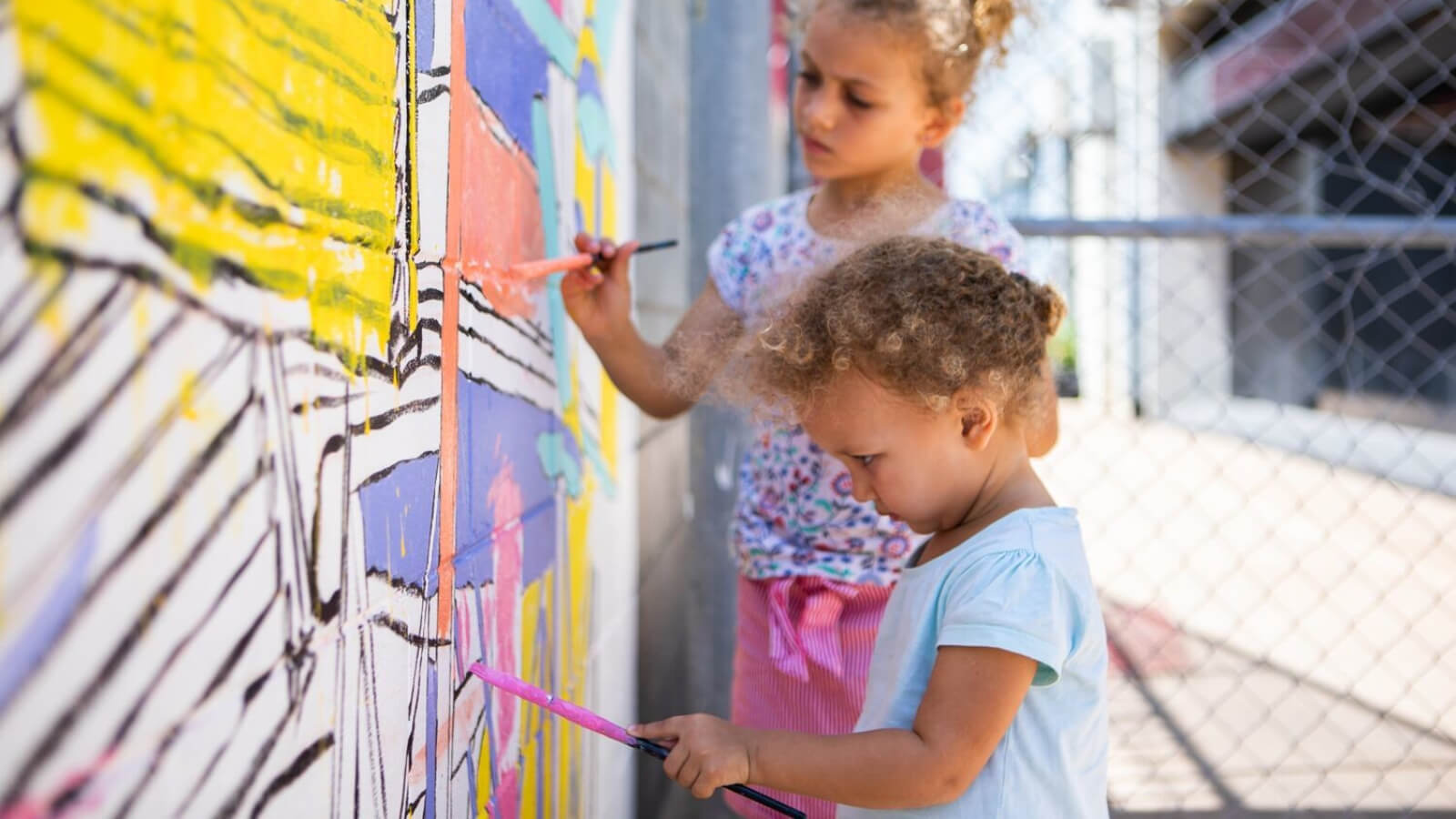 Children painting a wall on the street