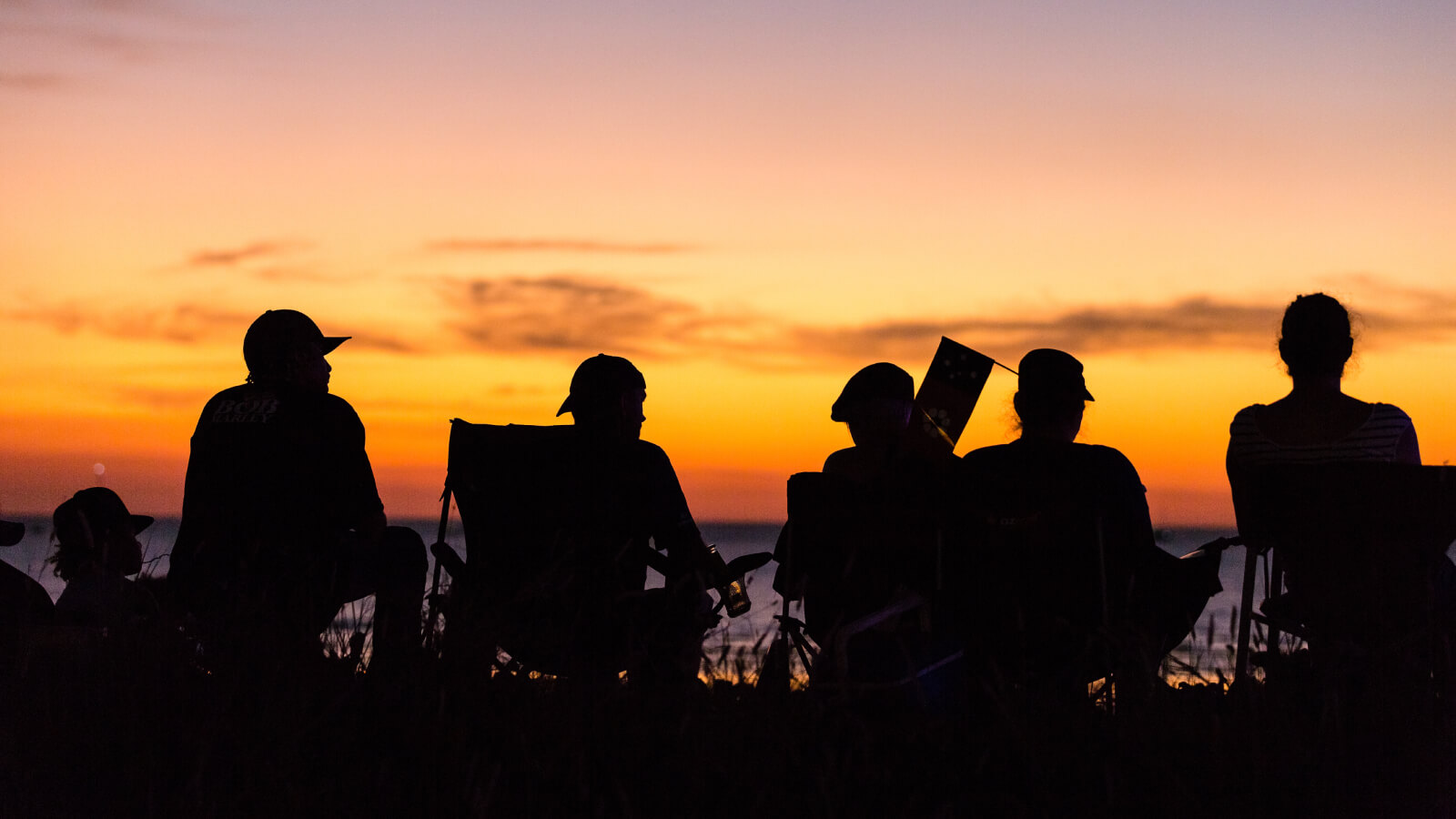 People sitting on chairs at the beach watching the sunset