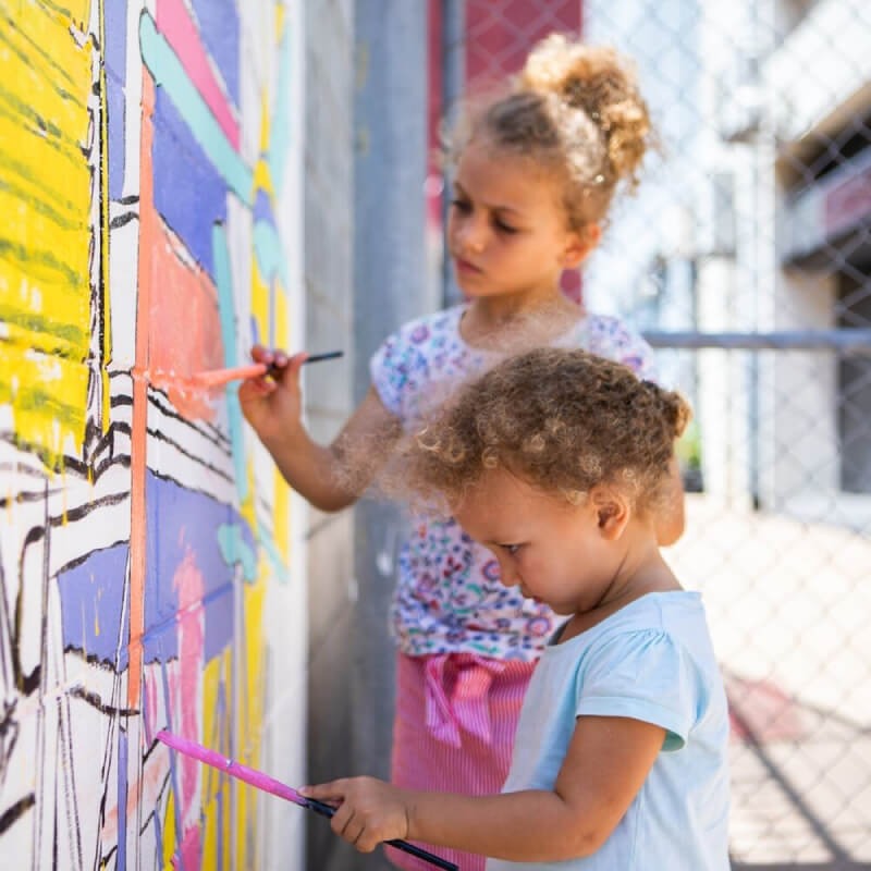 Children painting a wall on the street