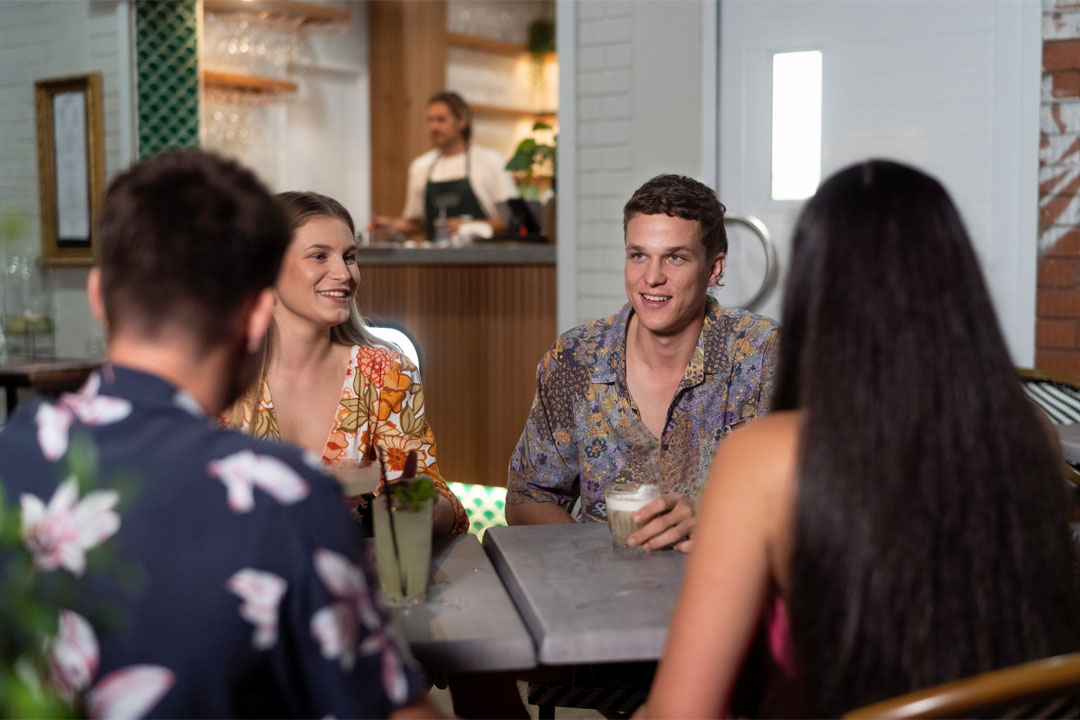two men and two women chat sitting at a bar