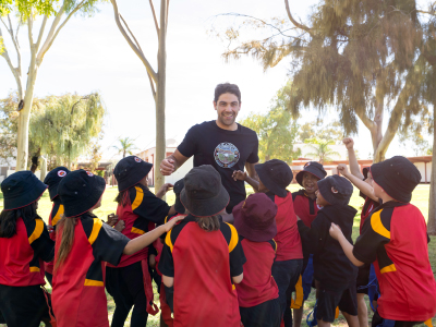 Teacher interacting with a group of children outdoors under trees in Alice Springs.